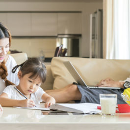 A mother and father sitting with their infant daughter as she draws in a notebook