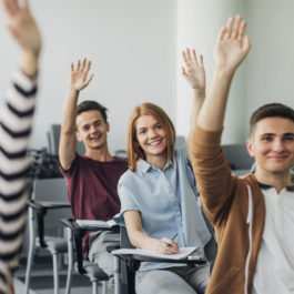 Happy teenagers raising their hands in class