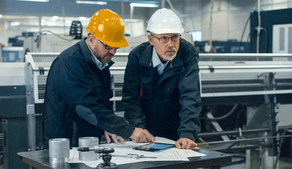 Two engineers looking at a tablet and schematics
