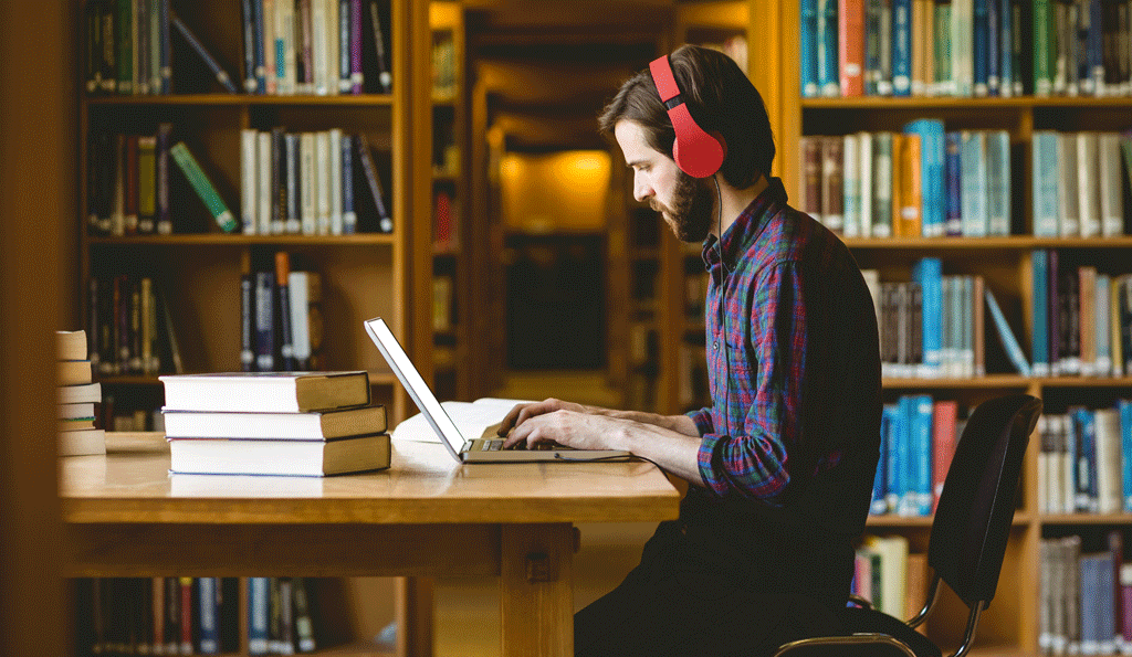 man wearing headphones and working on laptop in library